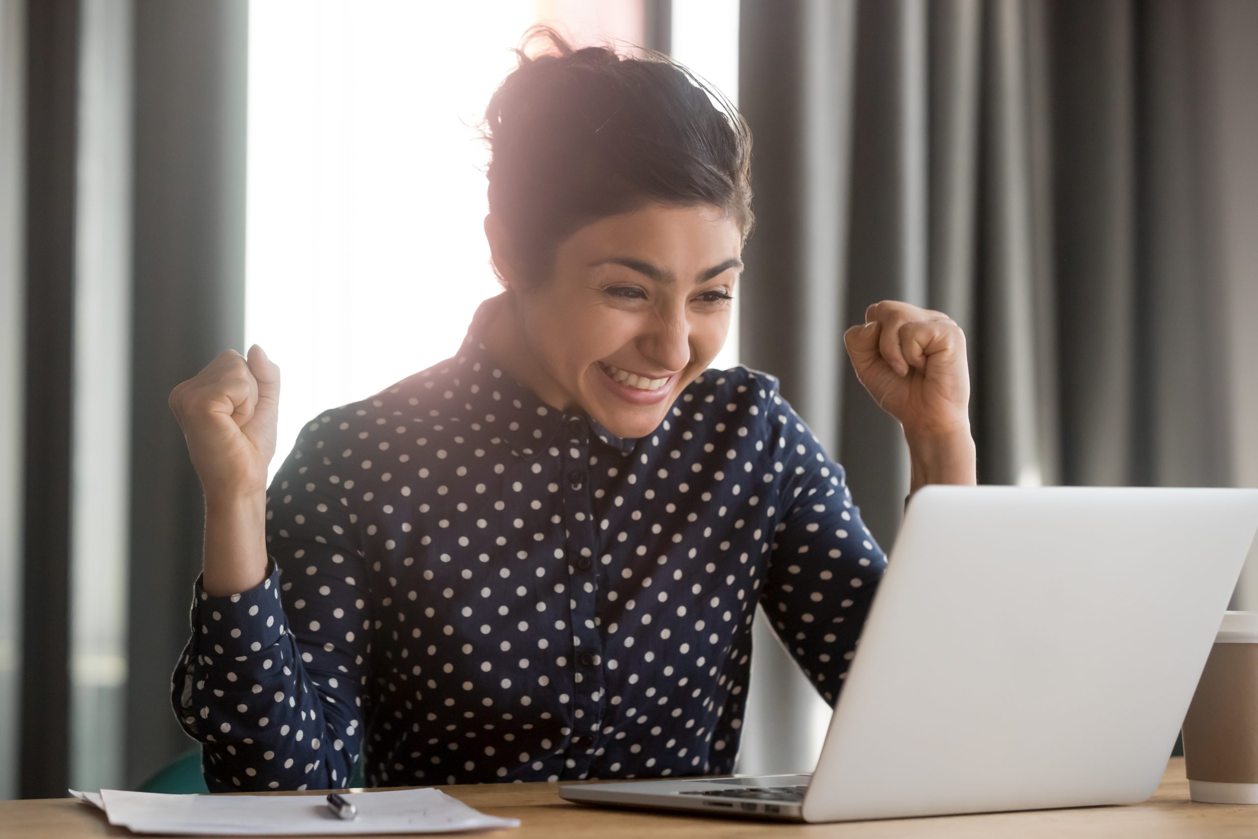 Excited young indian student receiving notification about hiring to work or unexpected good news. Happy successful female employee celebrating victory win achievement or job promoting.